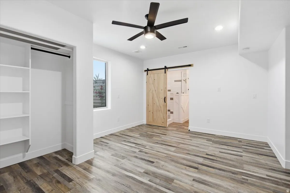 Wood-finish flooring, built-in shelving, a modern ceiling fan, and a wood barn door