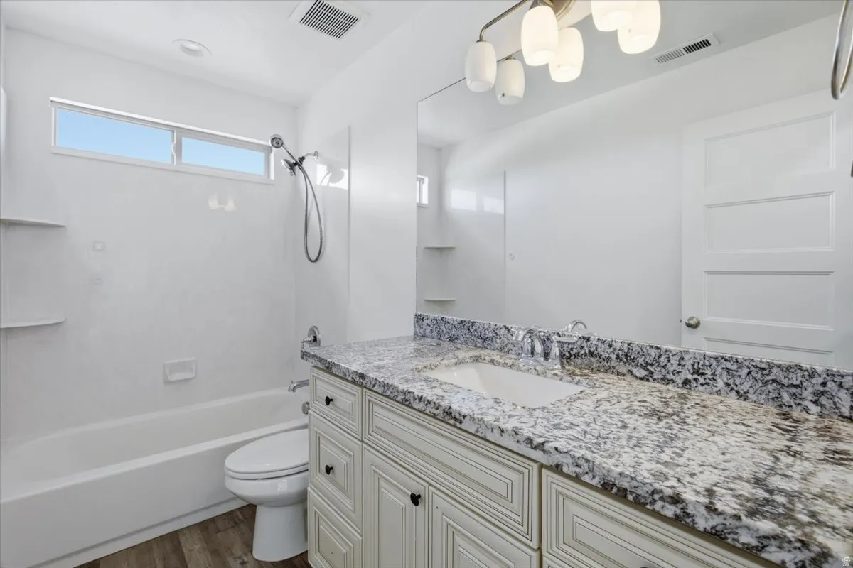 Bathroom featuring a single vanity with an integrated sink, granite countertop, and light-toned cabinetry