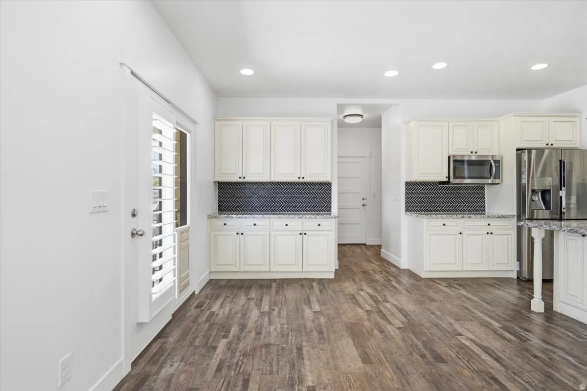 Open-concept kitchen featuring white cabinetry, stainless steel appliances, granite countertops, and a dark geometric tile backsplash