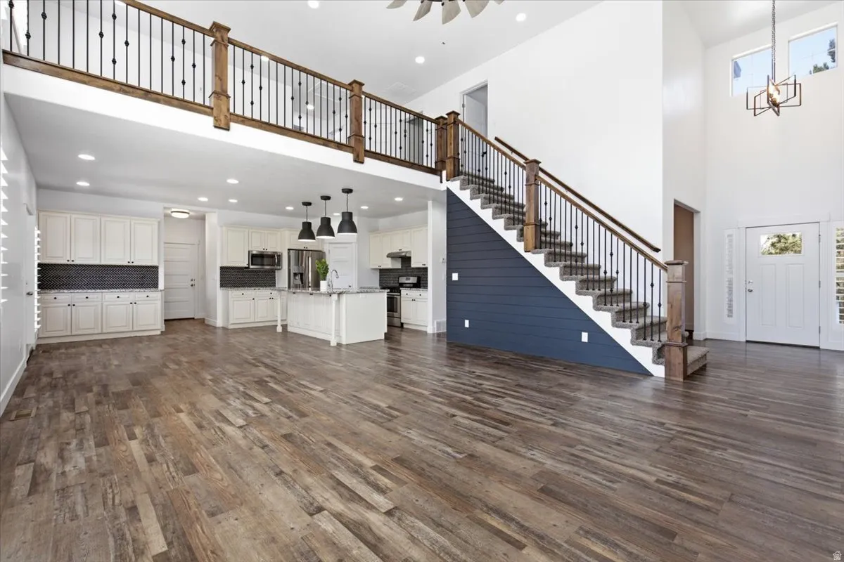 Vaulted ceilings with an open-concept layout, wood-finish flooring, white cabinetry, and a prominent staircase with dark wood and iron railings