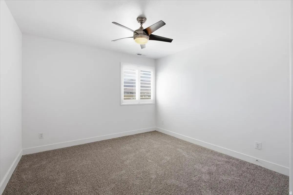 Plush carpeting, bright white walls, contemporary ceiling fan with light, and window with plantation shutters