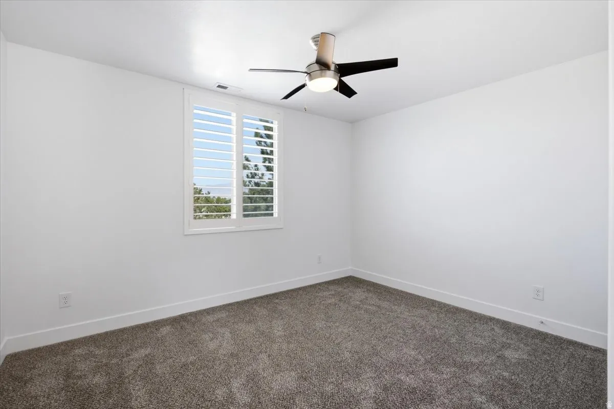 Recessed window with white plantation shutters, brushed nickel and black ceiling fan with integrated lighting, and neutral tone carpet flooring