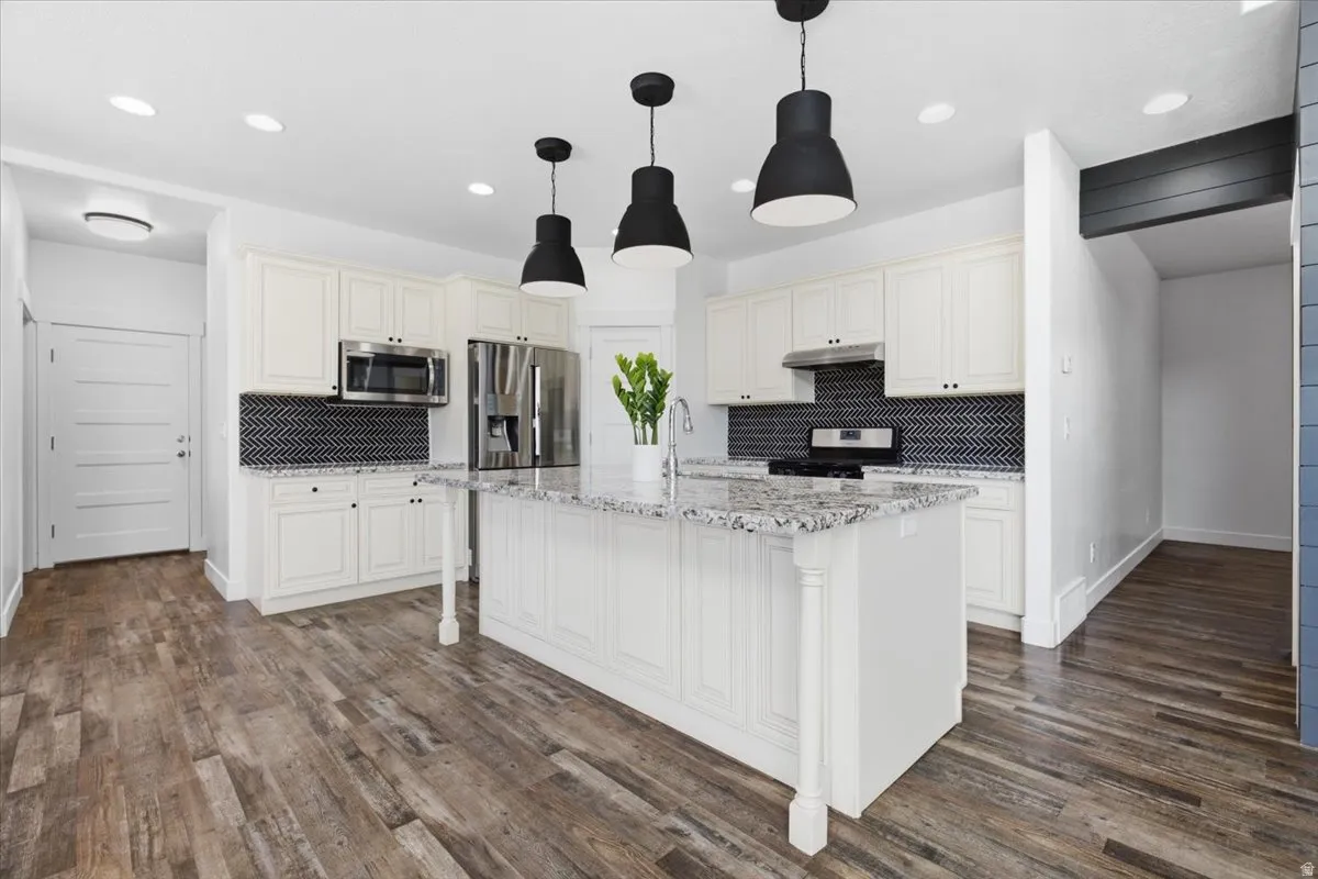 Kitchen featuring white cabinetry, a large central island with a stone countertop, a herringbone tile backsplash, and stainless steel appliances