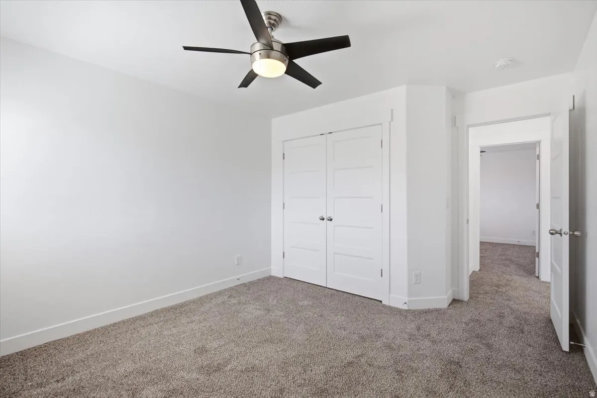 Neutral carpeted flooring, white walls, modern ceiling fan with lighting, white paneled bifold closet doors, and a white interior door