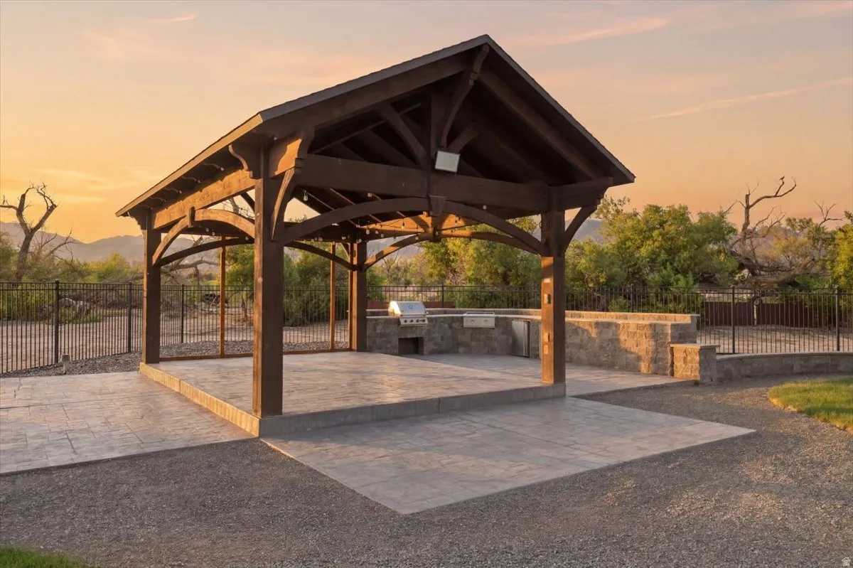 Expansive outdoor living area featuring a vaulted wood-beam gazebo, stone-faced built-in grill station, and a multi-level stamped concrete patio