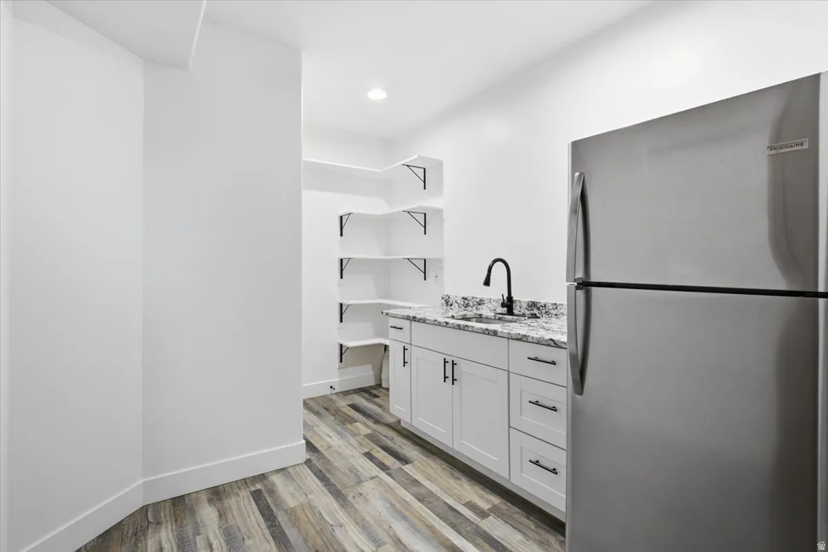 White cabinetry with black hardware, granite-style countertop, stainless steel refrigerator, black gooseneck faucet, and wood-finish flooring