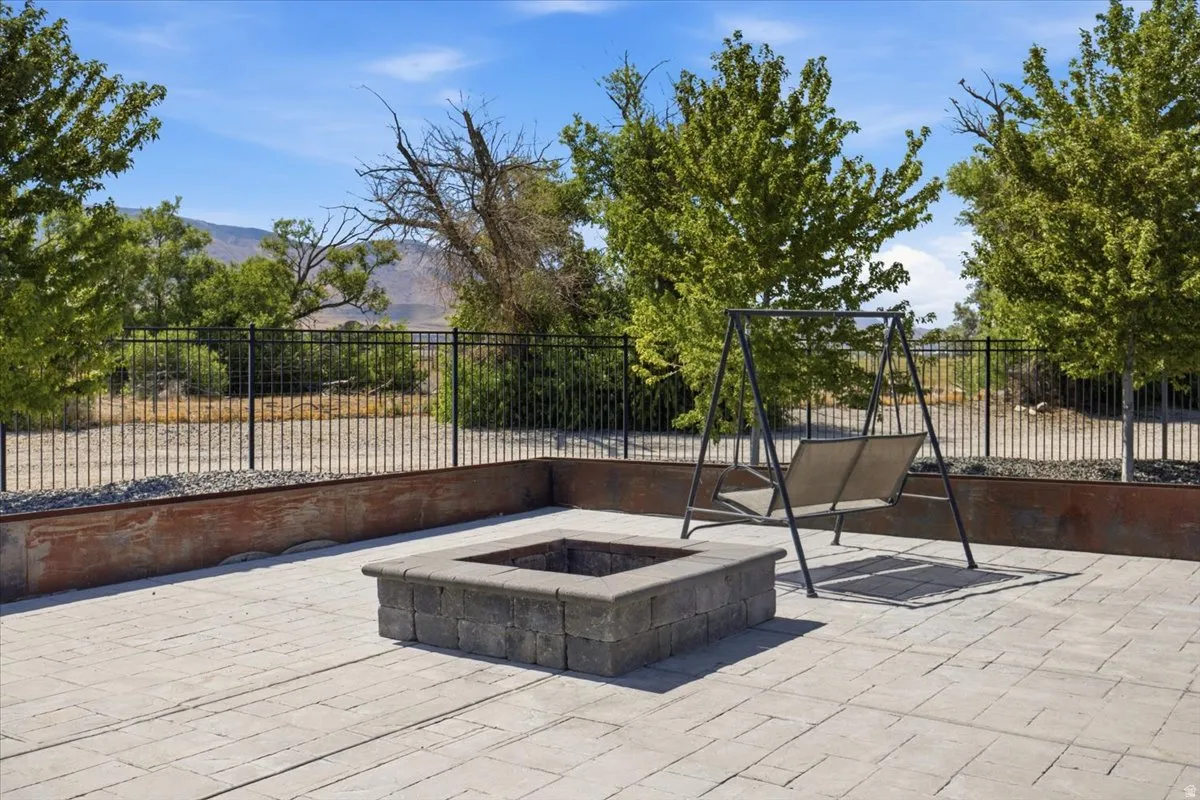 Paved patio with a built-in fire pit, surrounded by a metal fence, and mature trees