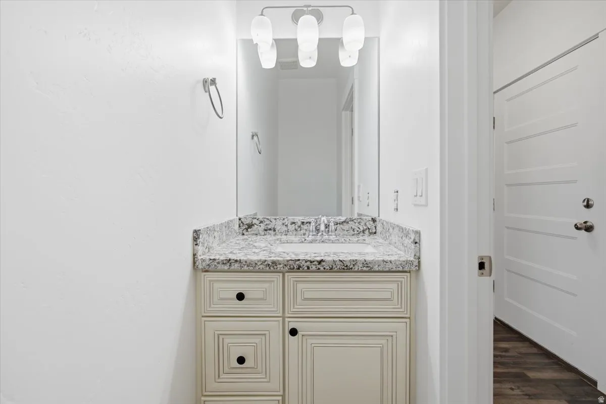 Cream-toned vanity with black hardware, stone-finish countertop, undermount sink, and wall-mounted light fixture