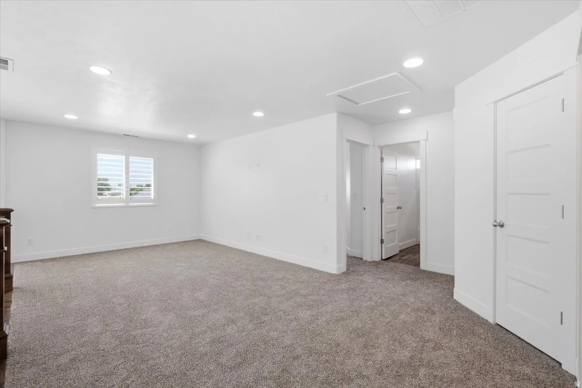 Expansive carpeted area featuring recessed lighting, white walls, multiple doorways, and a window with white shutters