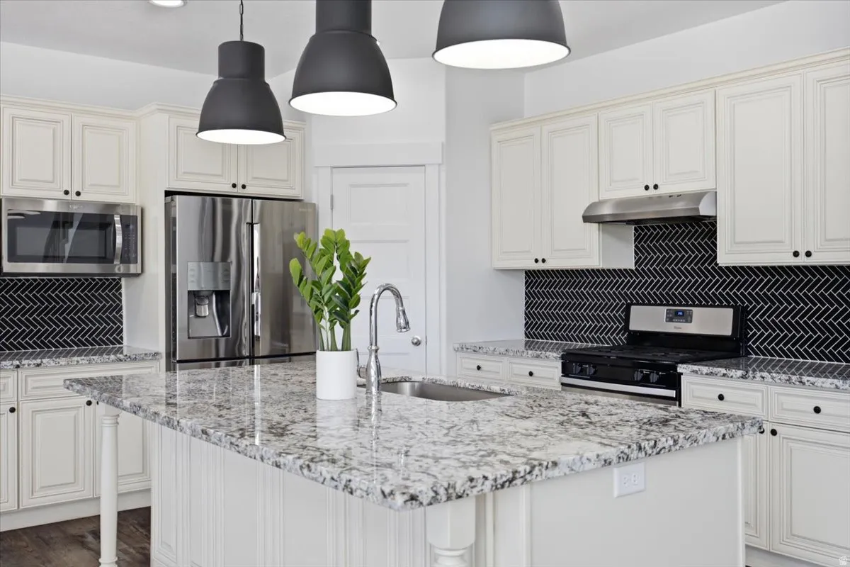Kitchen featuring a large island with a stainless steel sink, granite countertops, white cabinetry, and a black herringbone tile backsplash