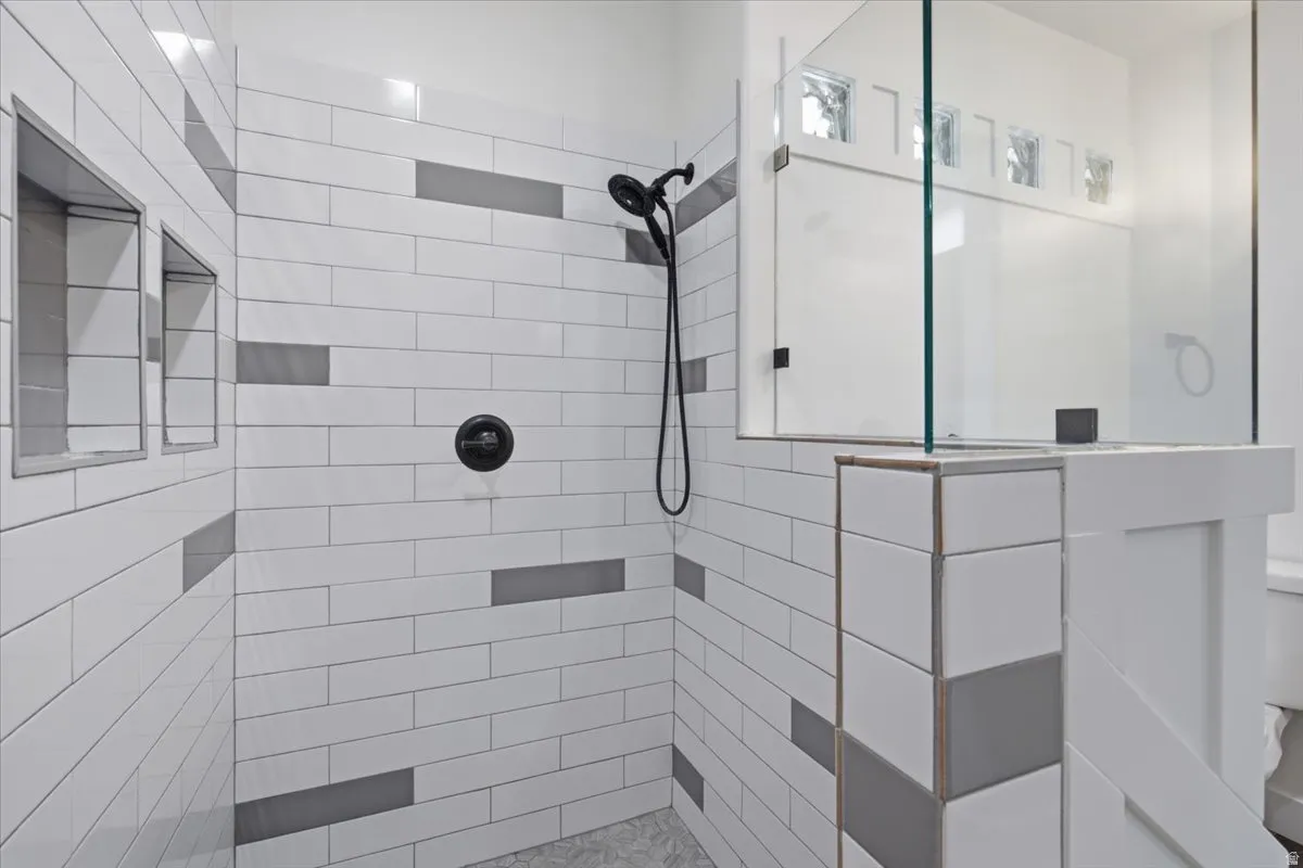 Shower with subway tile, glass enclosure, built-in recessed shelving, and a matte black shower system