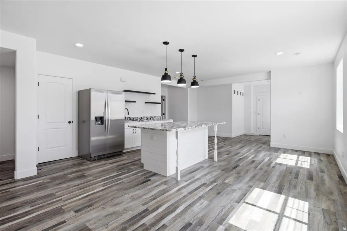 Open-concept living space with wood-finish flooring, a kitchen island featuring a stone countertop, recessed lighting, and stainless steel appliances