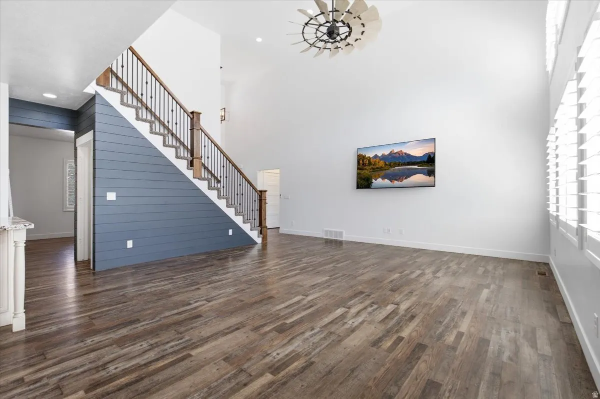 Spacious open-concept living area showcasing engineered wood-finish flooring, soaring vaulted ceilings with recessed lighting, and a blue-painted staircase with wooden railings