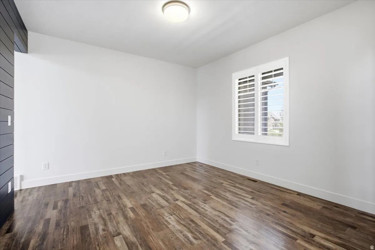 Wood-finish flooring, white walls, recessed window with white plantation shutters, and a flush mount ceiling light fixture