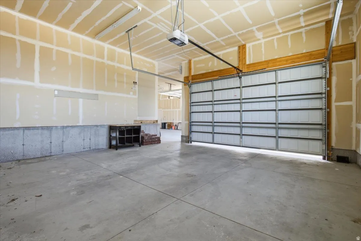 Concrete flooring, unfinished walls, exposed wooden beams, automatic garage door opener, fluorescent overhead lighting