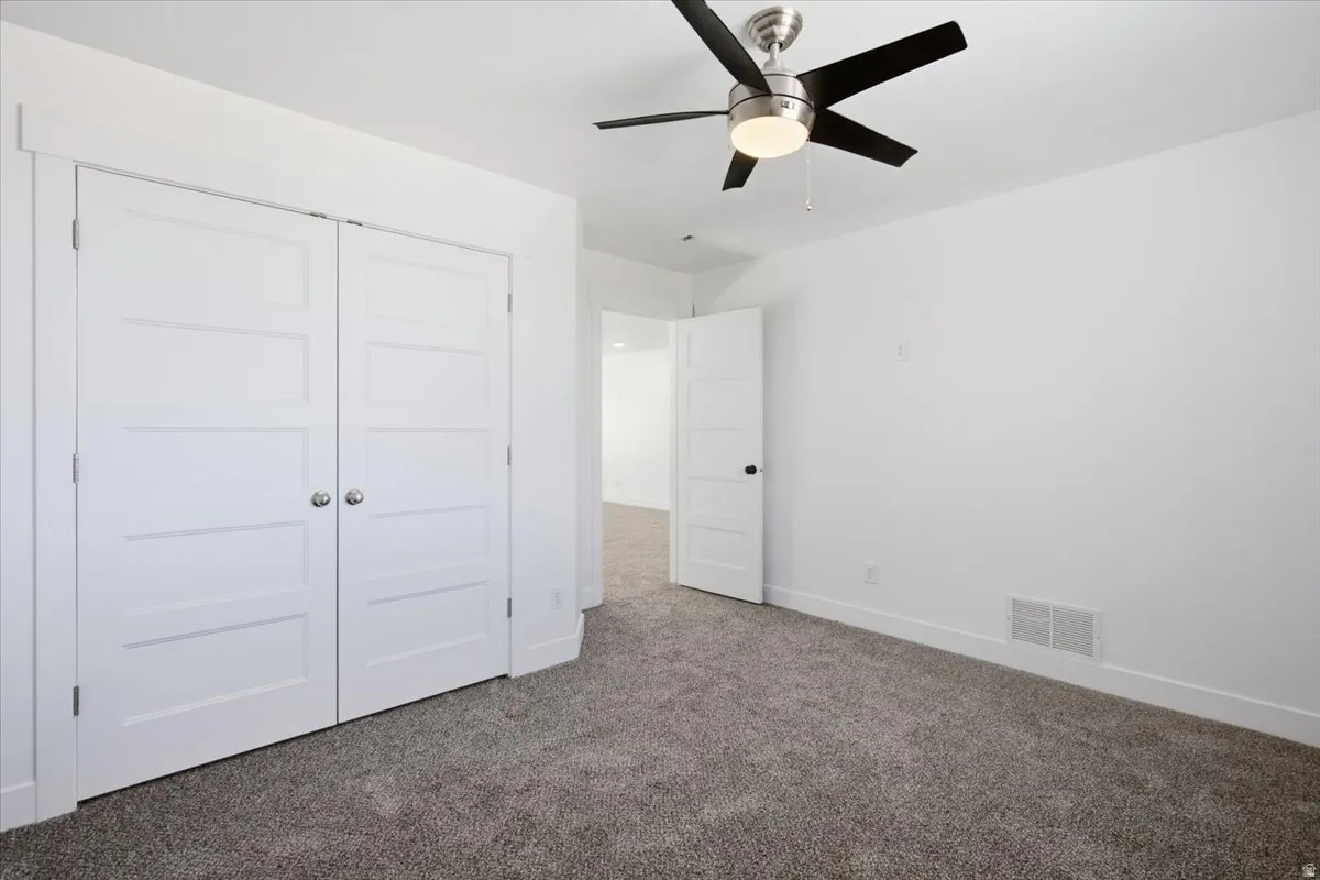 Plush grey carpet, modern ceiling fan with lighting, white four-panel doors, and crisp white walls