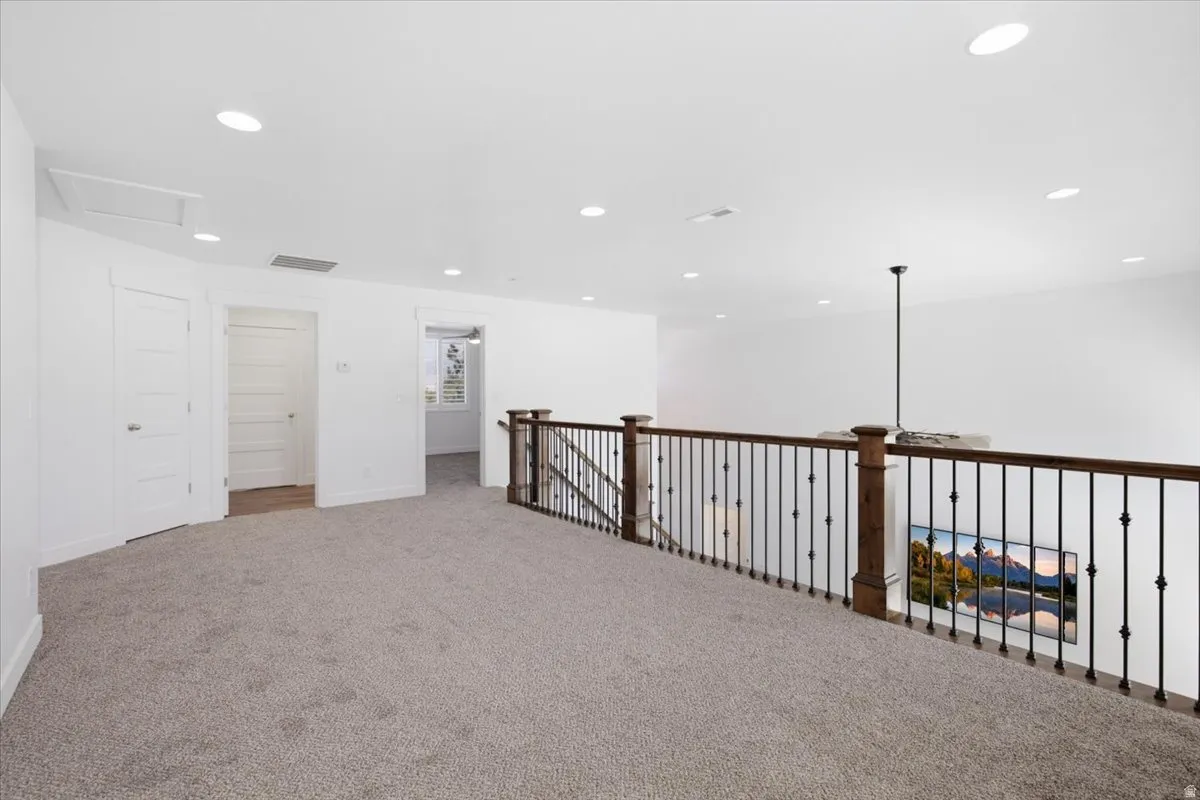Carpeted loft area featuring a wood and wrought iron railing, recessed lighting, and white paneled doors