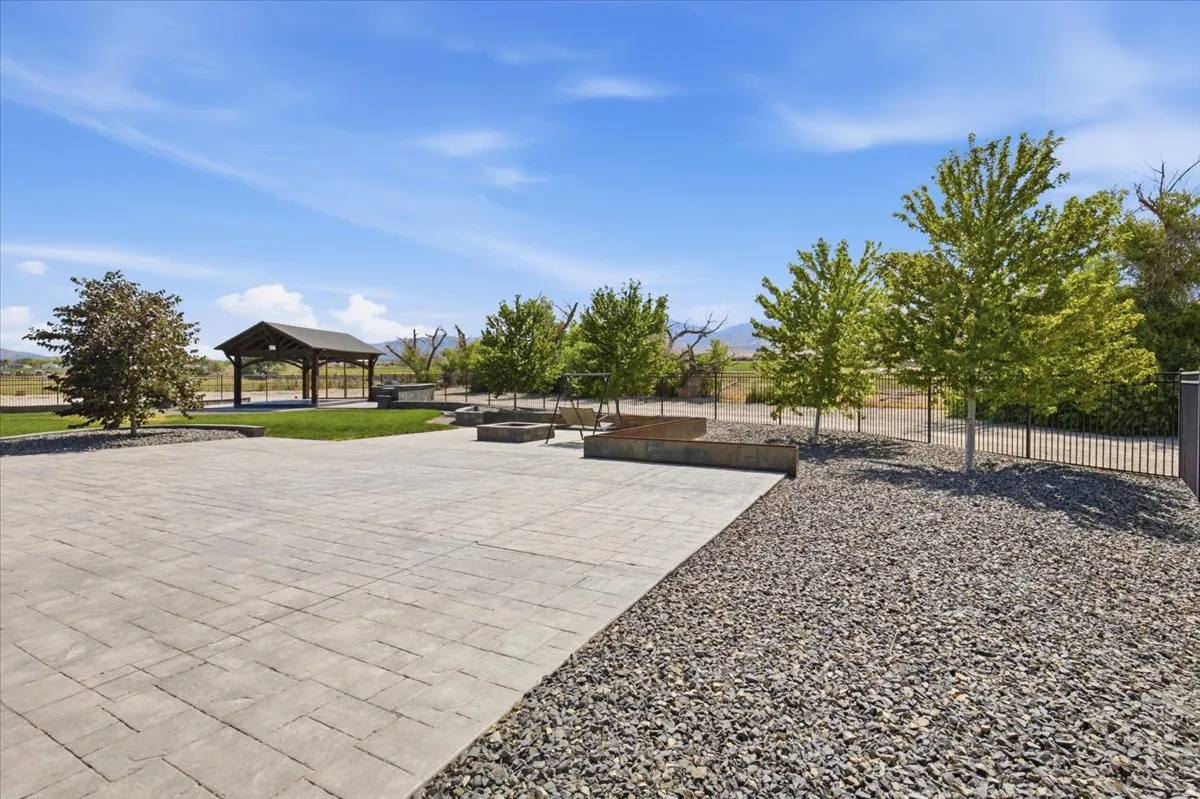 Expansive paved patio with an adjacent gravel bed, shaded gazebo, and mature trees