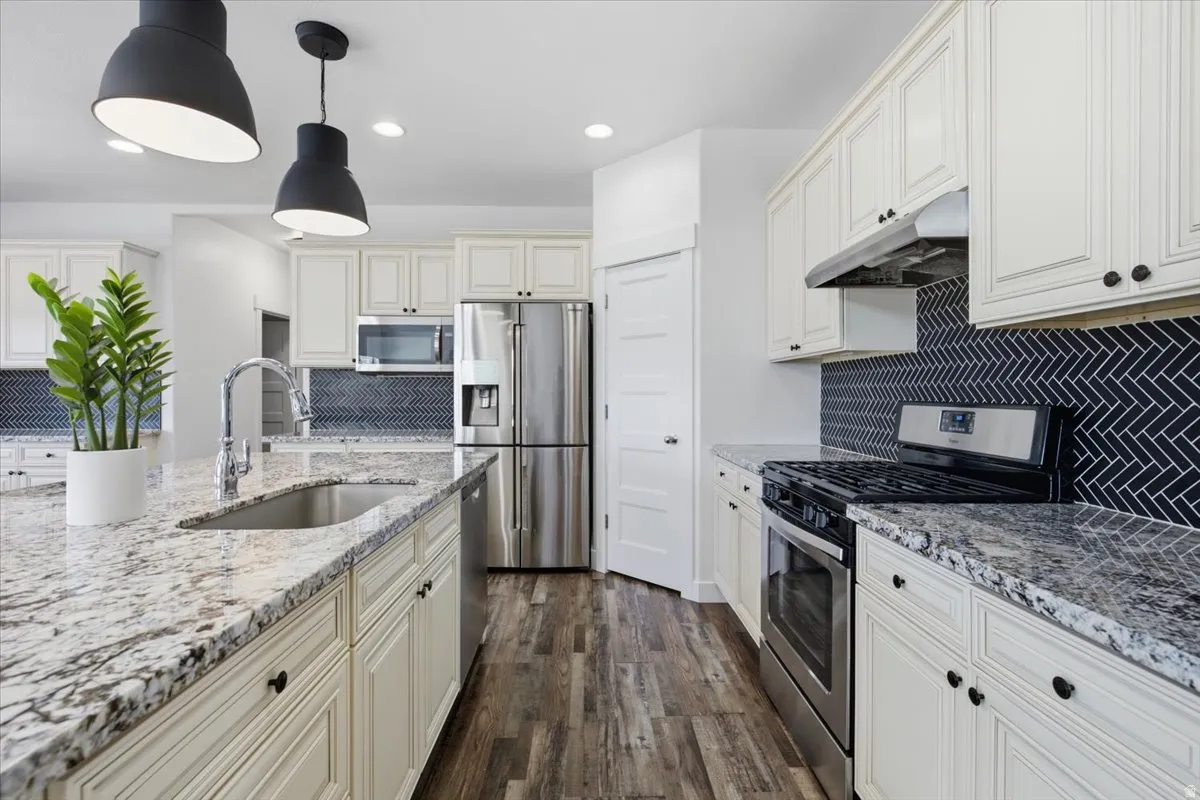 Gourmet kitchen featuring granite countertops, stainless steel appliances, white cabinetry, a herringbone tile backsplash, and wood-finish flooring