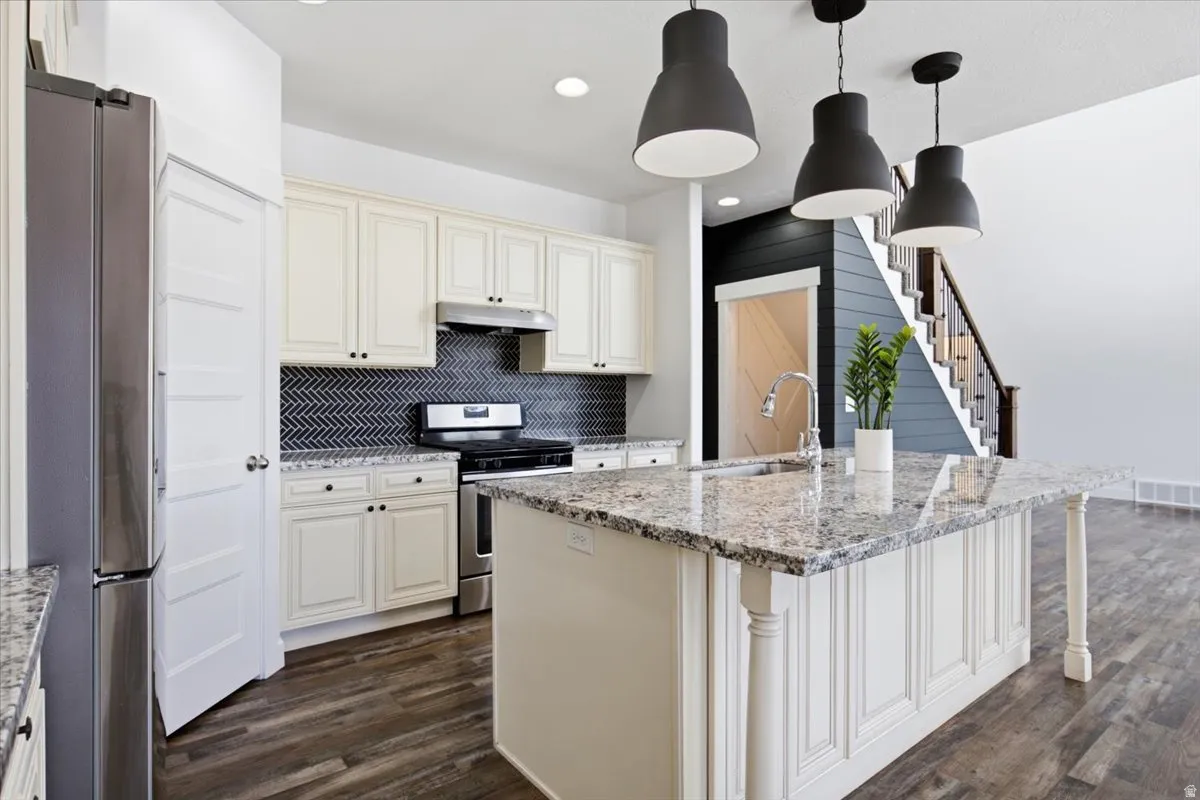 Kitchen featuring a central island with a built-in sink, granite countertops, stainless steel appliances, and a herringbone tile backsplash