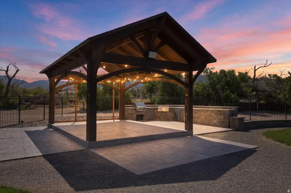 Covered outdoor structure with exposed wood beam construction, integrated barbecue, stone veneer built-in cabinetry, and stamped concrete patio