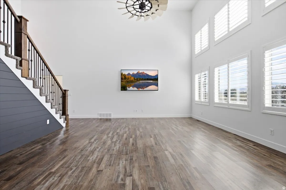 Two-story ceilings, wood-finish flooring, staircase with wood newel posts and metal balusters, and multiple windows with plantation shutters