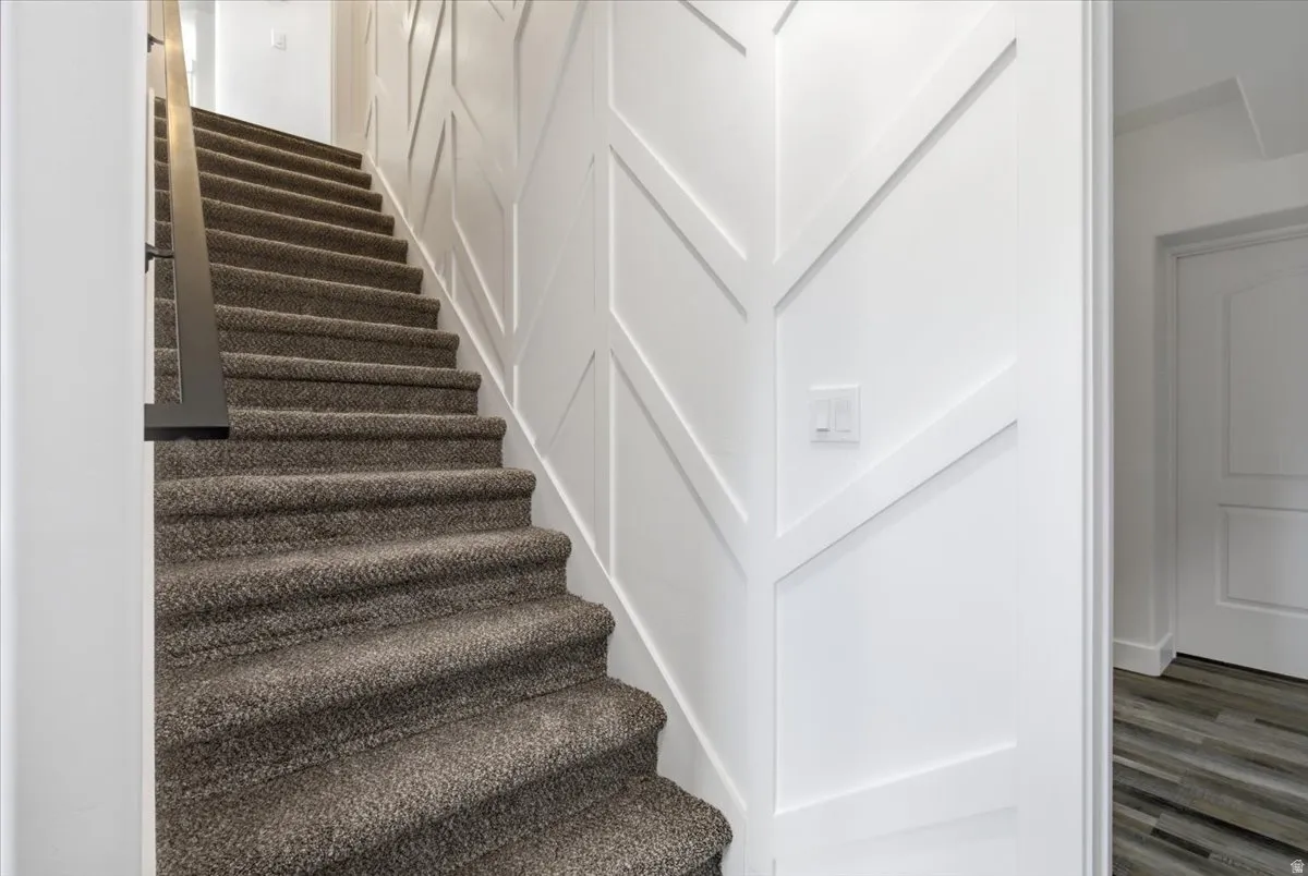 Carpeted staircase with a dark metal handrail, featuring decorative wall paneling and a white door frame