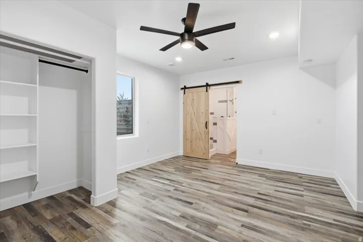 Wood-finish flooring, built-in shelving, a modern ceiling fan, and a wood barn door