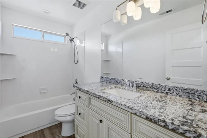 Bathroom featuring a single vanity with an integrated sink, granite countertop, and light-toned cabinetry