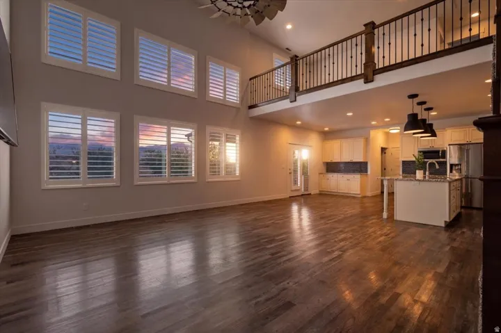 Open-concept living space featuring wood-finish flooring, a kitchen island with pendant lighting, white cabinetry, a stainless steel refrigerator, and a loft with a wrought iron railing