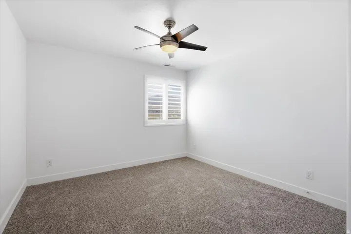 Plush carpeting, bright white walls, contemporary ceiling fan with light, and window with plantation shutters