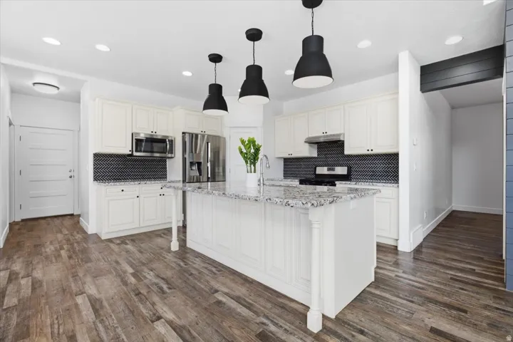 Kitchen featuring white cabinetry, a large central island with a stone countertop, a herringbone tile backsplash, and stainless steel appliances
