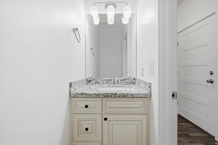 Cream-toned vanity with black hardware, stone-finish countertop, undermount sink, and wall-mounted light fixture