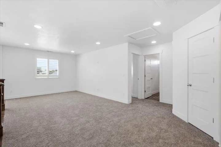 Expansive carpeted area featuring recessed lighting, white walls, multiple doorways, and a window with white shutters
