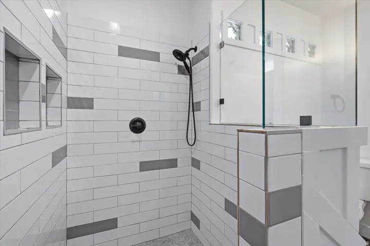 Shower with subway tile, glass enclosure, built-in recessed shelving, and a matte black shower system