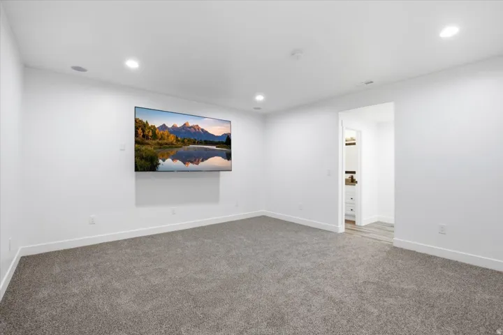 Recessed lighting, wall-mounted television, and speaker system with neutral carpeting