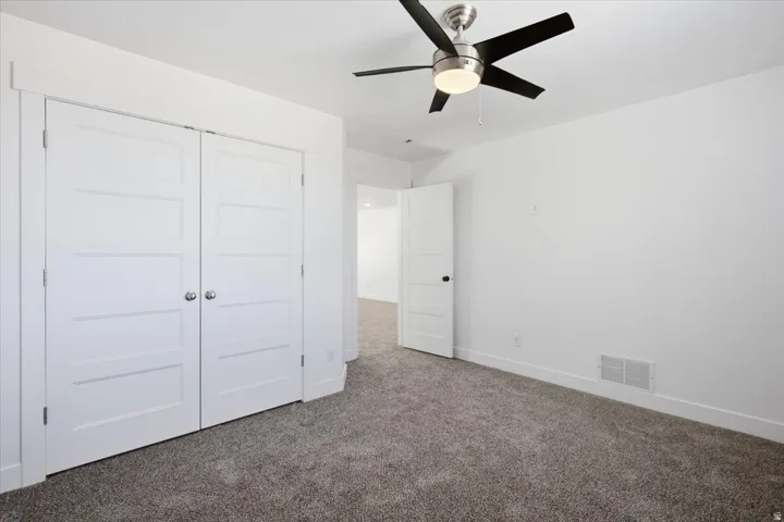 Plush grey carpet, modern ceiling fan with lighting, white four-panel doors, and crisp white walls