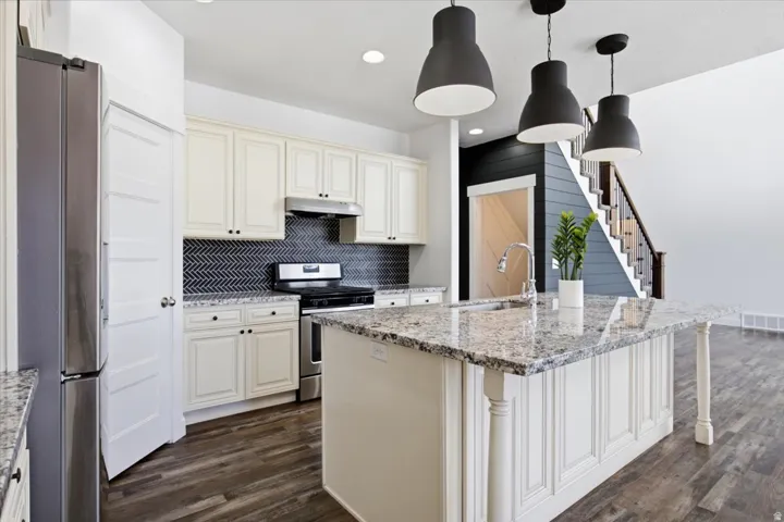 Kitchen featuring a central island with a built-in sink, granite countertops, stainless steel appliances, and a herringbone tile backsplash