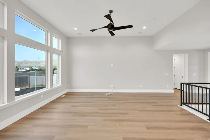 Expansive room featuring multiple large windows, wood-finish flooring, a modern ceiling fan, recessed lighting, and an open metal railing