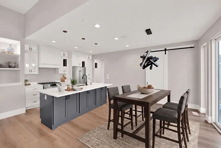 Expansive kitchen featuring a two-toned island with ample counter space, stainless steel appliances, and a modern dining area with a unique chandelier