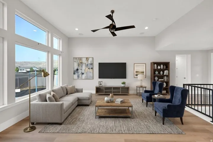 Expansive living area featuring soaring ceilings, a modern ceiling fan, recessed lighting, large windows, and wood-finish flooring