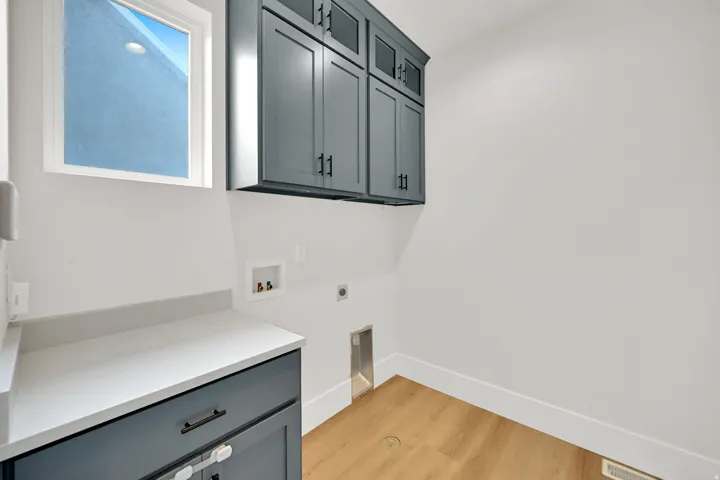 Modern kitchen featuring custom dark cabinetry with hardware accents, white quartz countertops, stainless steel appliances, and warm wood-finish flooring throughout the space