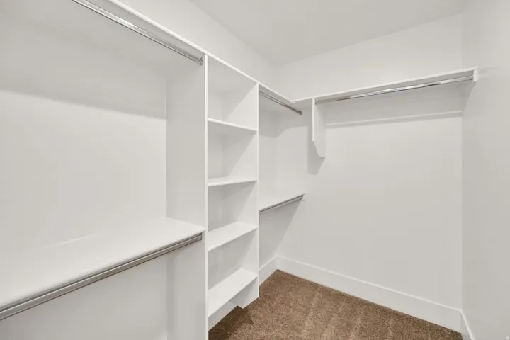Walk-in closet with integrated shelving, multiple hanging rods, and carpet flooring