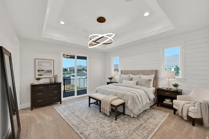 Spacious primary bedroom featuring shiplap accent walls, coffered ceiling with integrated lighting, dual nightstands with dark wood finishes, and glass sliding doors opening to a private balcony with water and cityscape backdrop