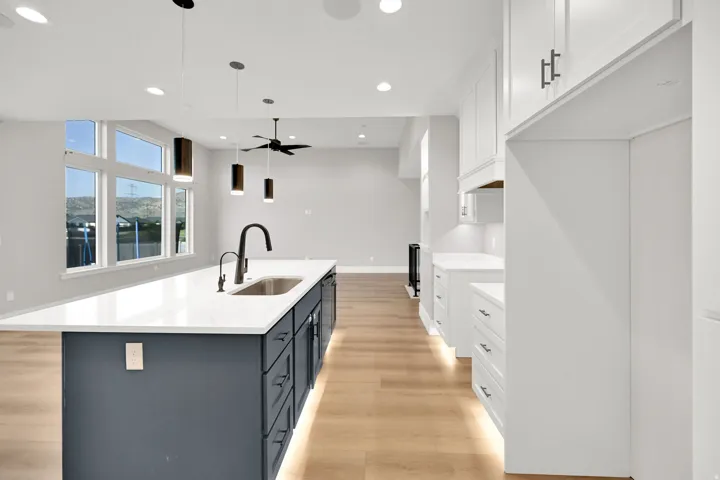 Spacious kitchen featuring a large island with an undermount sink and matte black faucet, pendant lighting, recessed lighting, white cabinetry, and wood-finish flooring