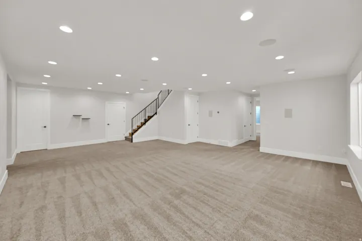 Expansive carpeted area with recessed lighting, multiple white panel doors, and a staircase featuring black metal railings