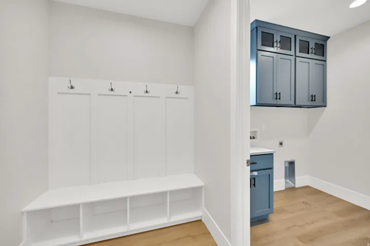 Dedicated mudroom featuring custom white cabinetry with individual cubbies and open shelving, paired with wood-finish flooring