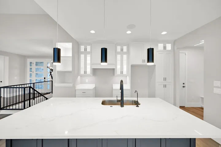 Expansive kitchen island with white quartz countertop and waterfall edge, paired with matte black pendant lighting and matching faucet