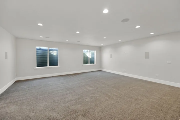 Recessed lighting throughout, two windows, wall-mounted speakers, and gray carpeting