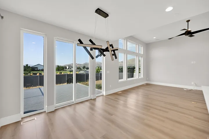 Bright, open room featuring expansive glass doors and windows with sightlines to outdoor space, light wood-finish flooring throughout, ceiling fan with integrated lighting, and recessed ceiling fixtures